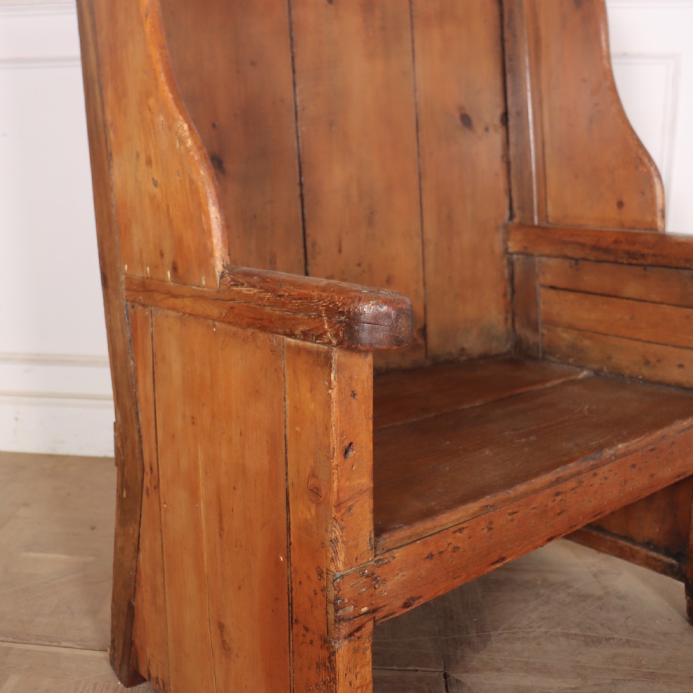 A high-backed antique pine wooden settle featuring tall vertical plank panels, curved side wings, and a floral upholstered seat cushion. View VII
