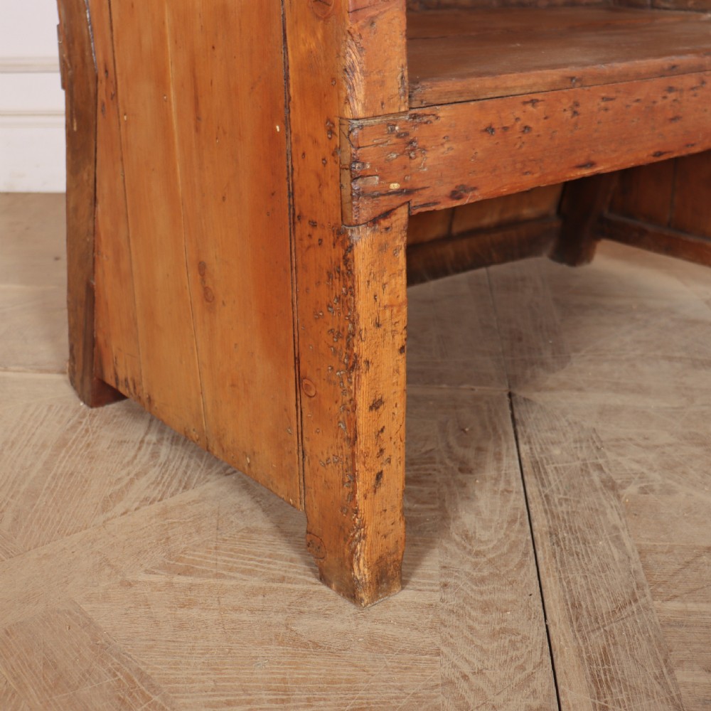 A high-backed antique pine wooden settle featuring tall vertical plank panels, curved side wings, and a floral upholstered seat cushion. View VIII