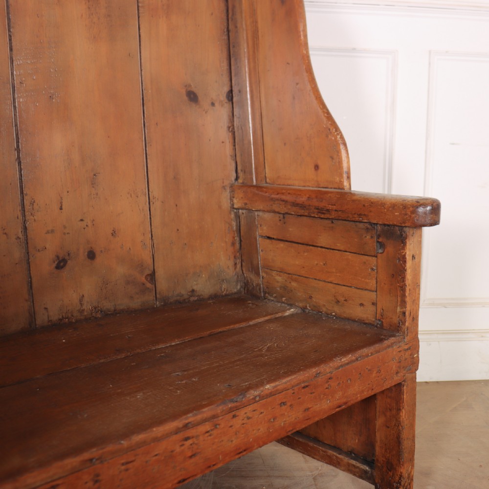 A high-backed antique pine wooden settle featuring tall vertical plank panels, curved side wings, and a floral upholstered seat cushion. View IX