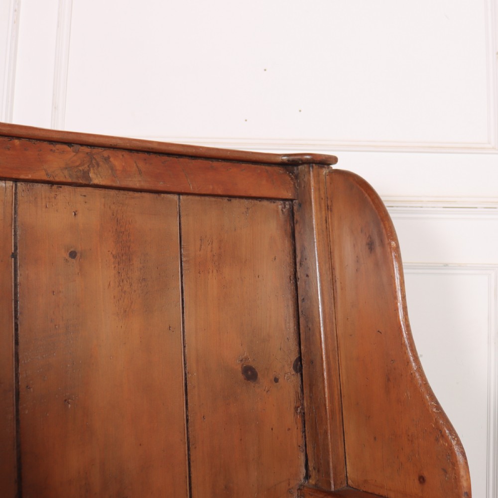 A high-backed antique pine wooden settle featuring tall vertical plank panels, curved side wings, and a floral upholstered seat cushion. View X