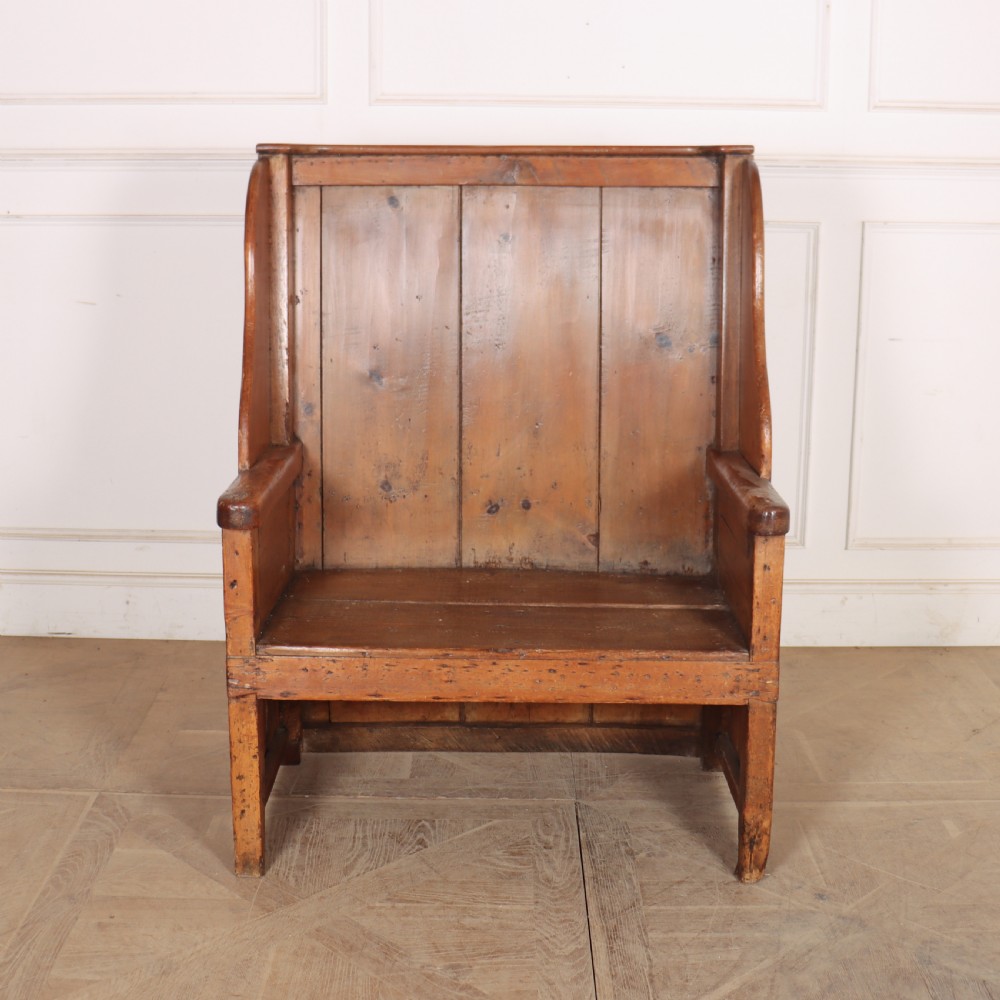 A high-backed antique pine wooden settle featuring tall vertical plank panels, curved side wings, and a floral upholstered seat cushion. View XI