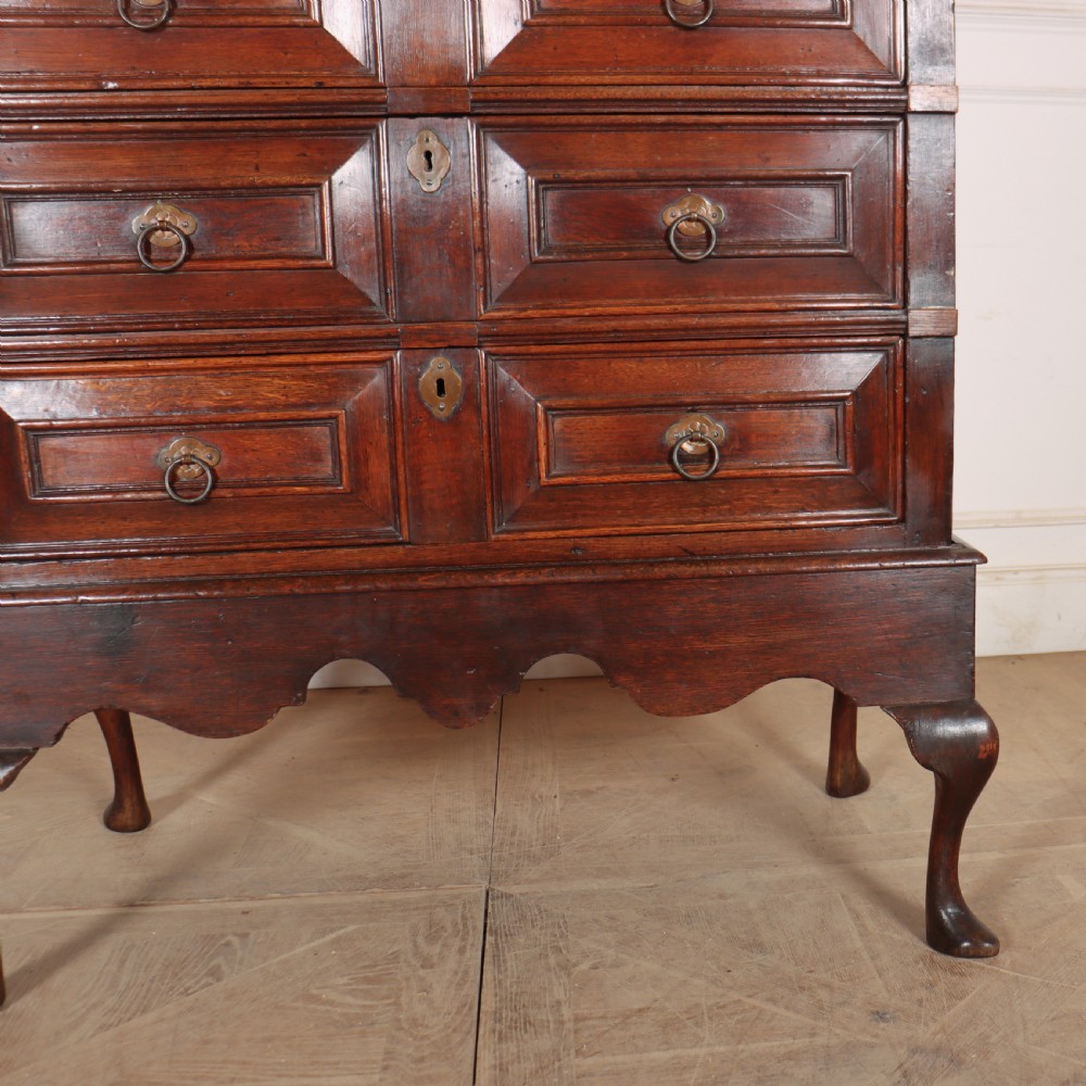 A warm brown wooden antique chest on stand with geometric moulded drawer fronts, brass drop handles, and slender cabriole legs. View V