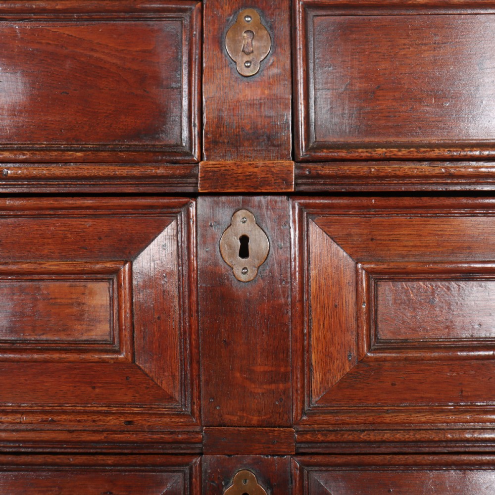 A warm brown wooden antique chest on stand with geometric moulded drawer fronts, brass drop handles, and slender cabriole legs. View VII