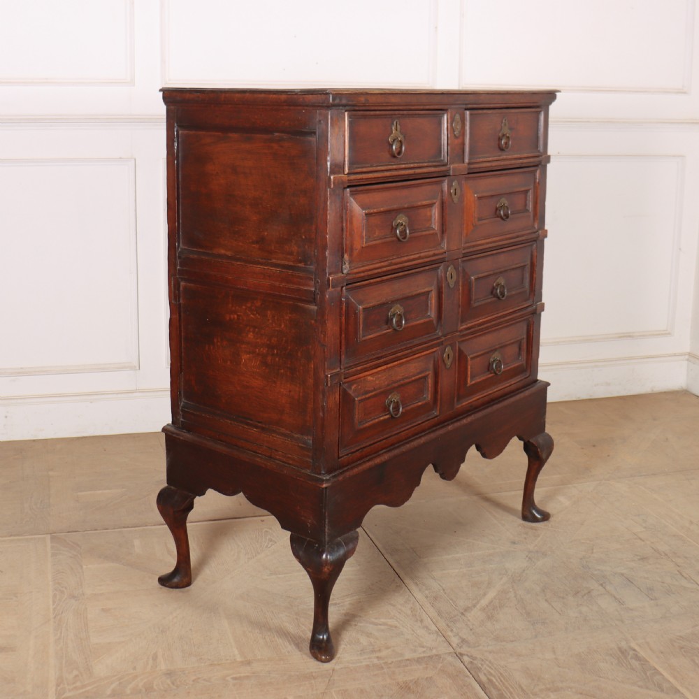 A warm brown wooden antique chest on stand with geometric moulded drawer fronts, brass drop handles, and slender cabriole legs. View IX