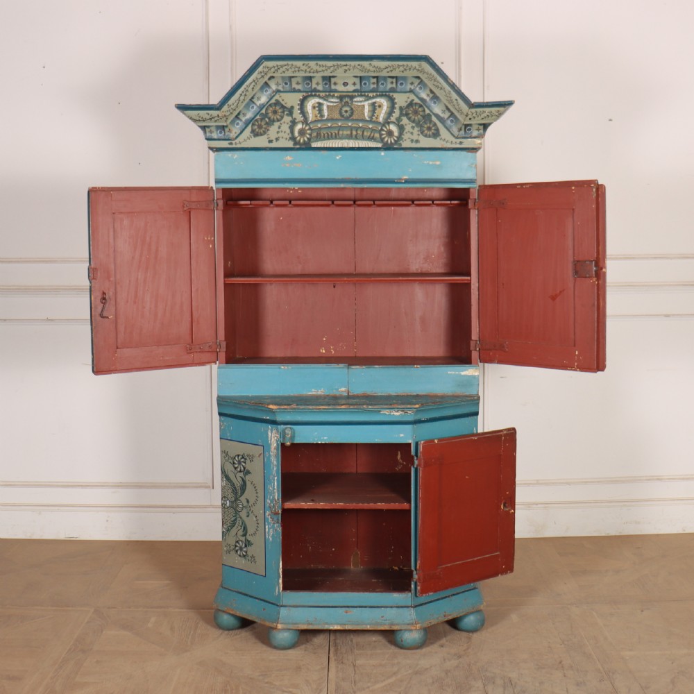 A tall two-tier Gustavian painted pine cabinet featuring a distressed blue finish, hand-painted urn panels, a shaped pediment with date inscription, and turned bun feet. View III