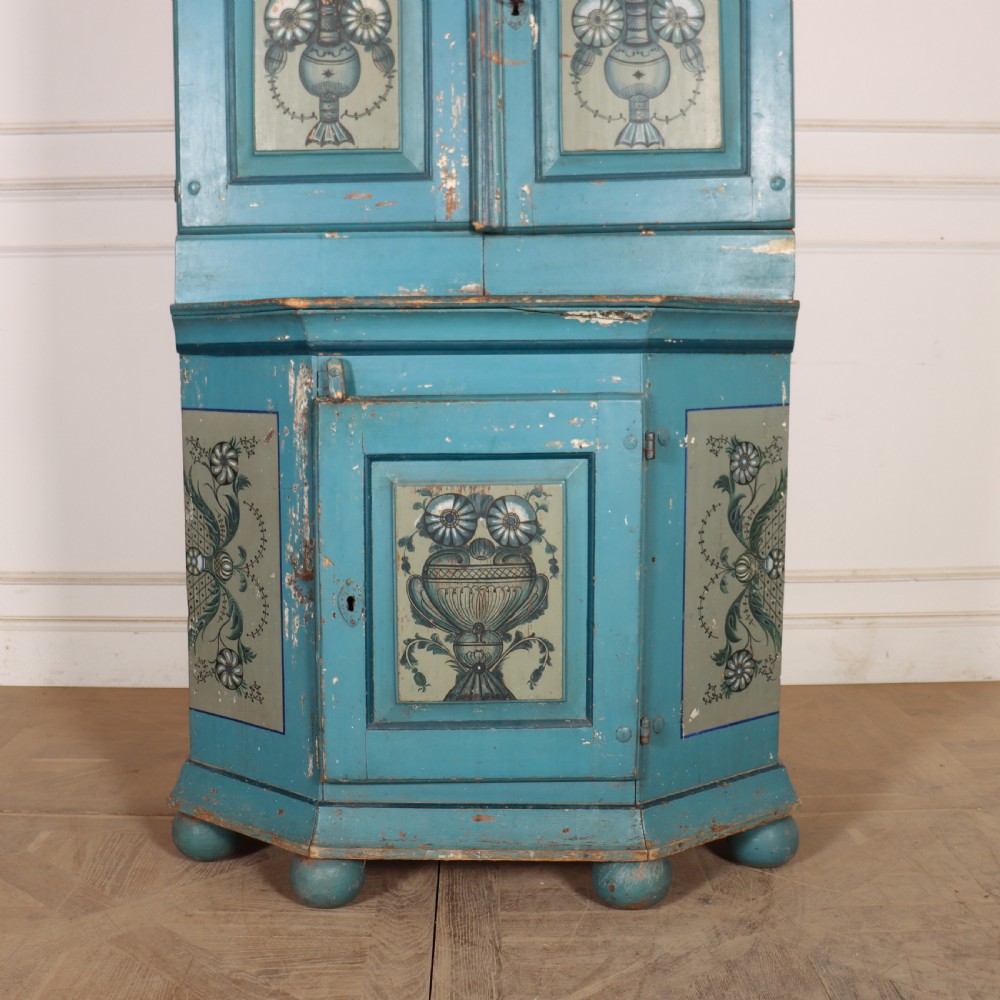 A tall two-tier Gustavian painted pine cabinet featuring a distressed blue finish, hand-painted urn panels, a shaped pediment with date inscription, and turned bun feet. View IV