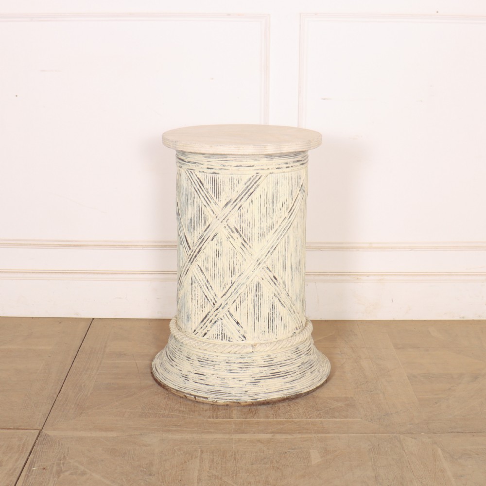 A cylindrical off-white painted wooden sculpture stand featuring carved cross-hatching patterns, a rope-twist lower border, and a distressed finish.