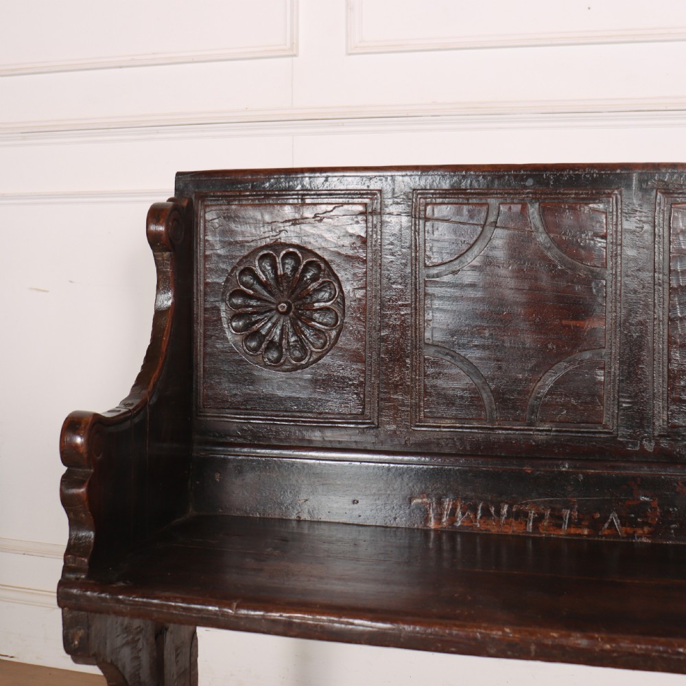 A dark brown carved walnut bench with a panelled backrest featuring carved rosette medallions and detailed carved feet. View II