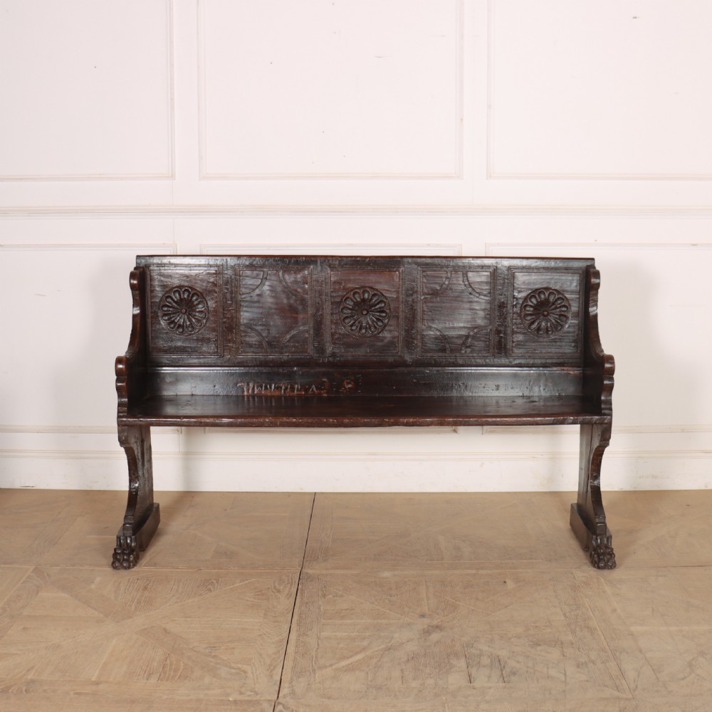 A dark brown carved walnut bench with a panelled backrest featuring carved rosette medallions and detailed carved feet.
