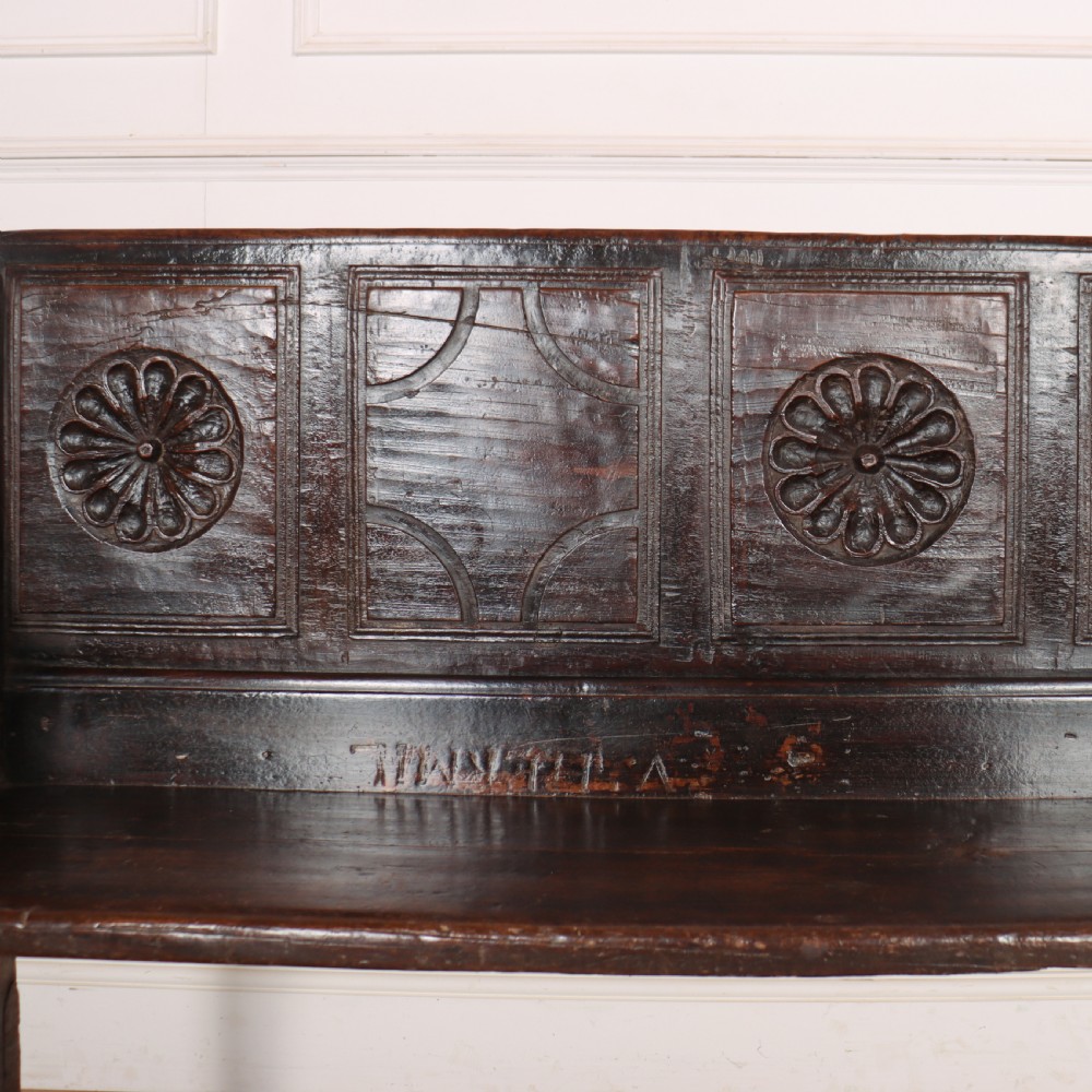 A dark brown carved walnut bench with a panelled backrest featuring carved rosette medallions and detailed carved feet. View III