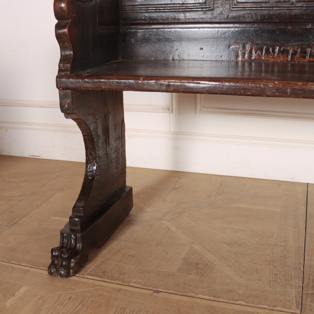 A dark brown carved walnut bench with a panelled backrest featuring carved rosette medallions and detailed carved feet. View VII