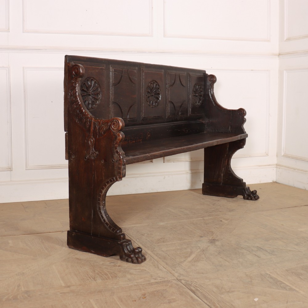 A dark brown carved walnut bench with a panelled backrest featuring carved rosette medallions and detailed carved feet. View VIII