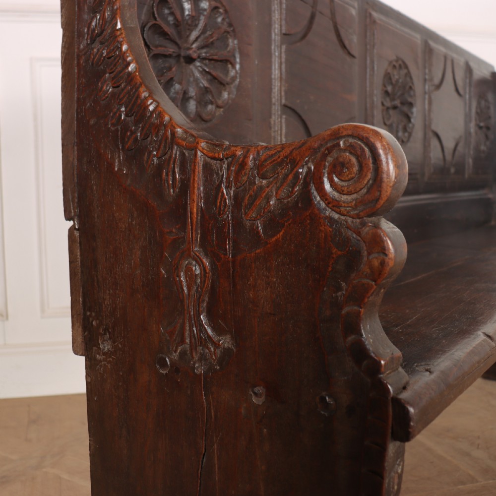 A dark brown carved walnut bench with a panelled backrest featuring carved rosette medallions and detailed carved feet. View XI