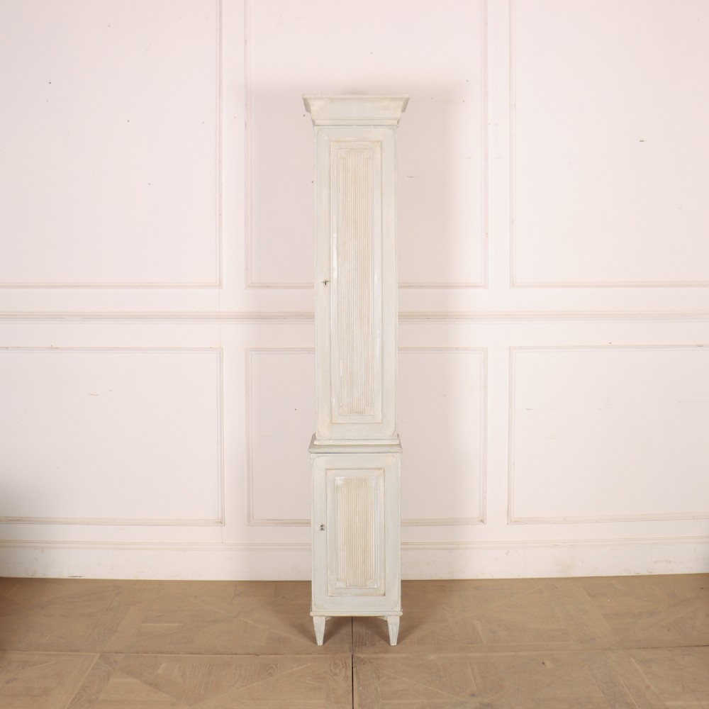 A tall, narrow Gustavian style two-tier painted wooden cabinet in pale grey with fluted panel doors and tapered feet.
