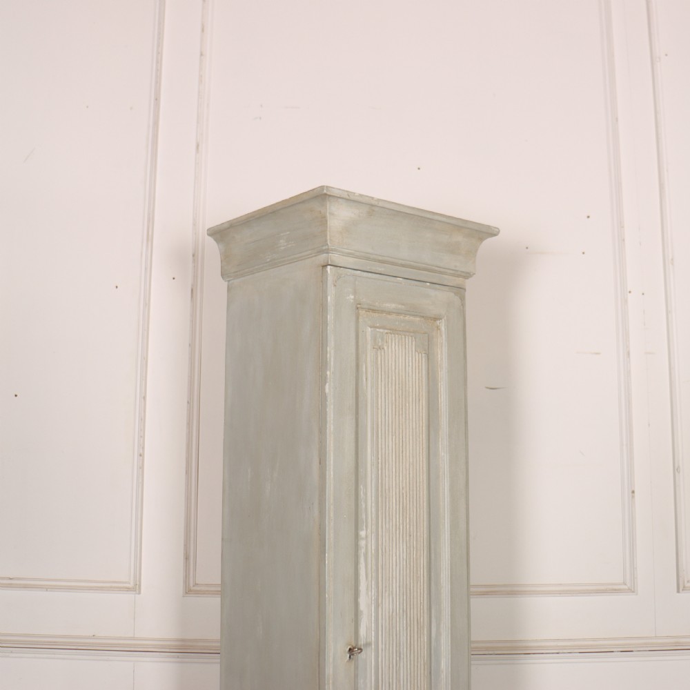 A tall, narrow Gustavian style two-tier painted wooden cabinet in pale grey with fluted panel doors and tapered feet. View III