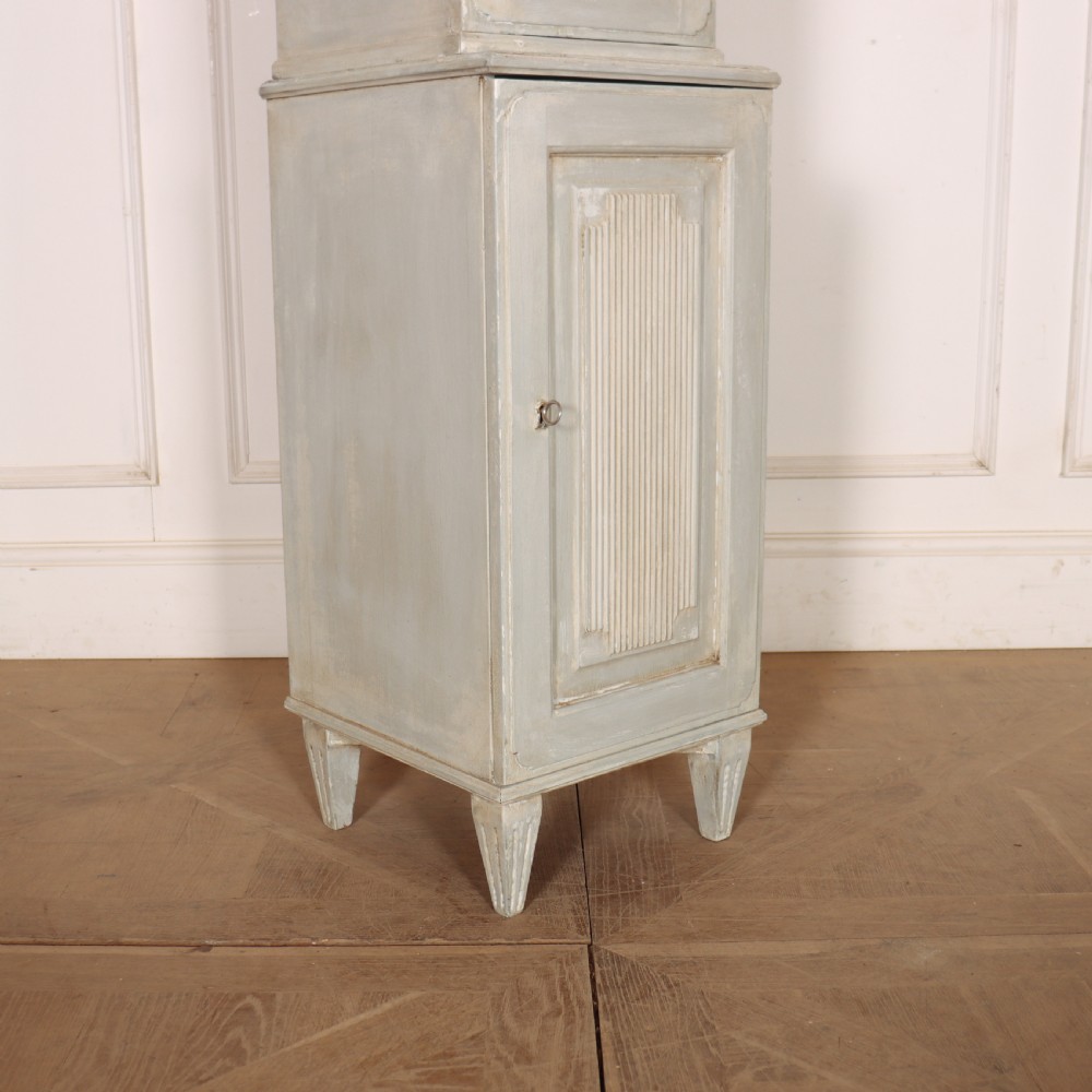 A tall, narrow Gustavian style two-tier painted wooden cabinet in pale grey with fluted panel doors and tapered feet. View V