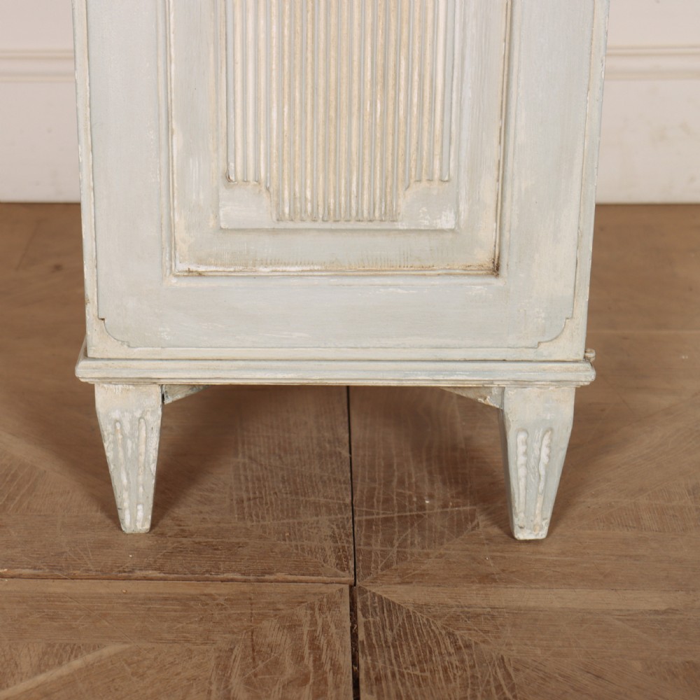 A tall, narrow Gustavian style two-tier painted wooden cabinet in pale grey with fluted panel doors and tapered feet. View VII