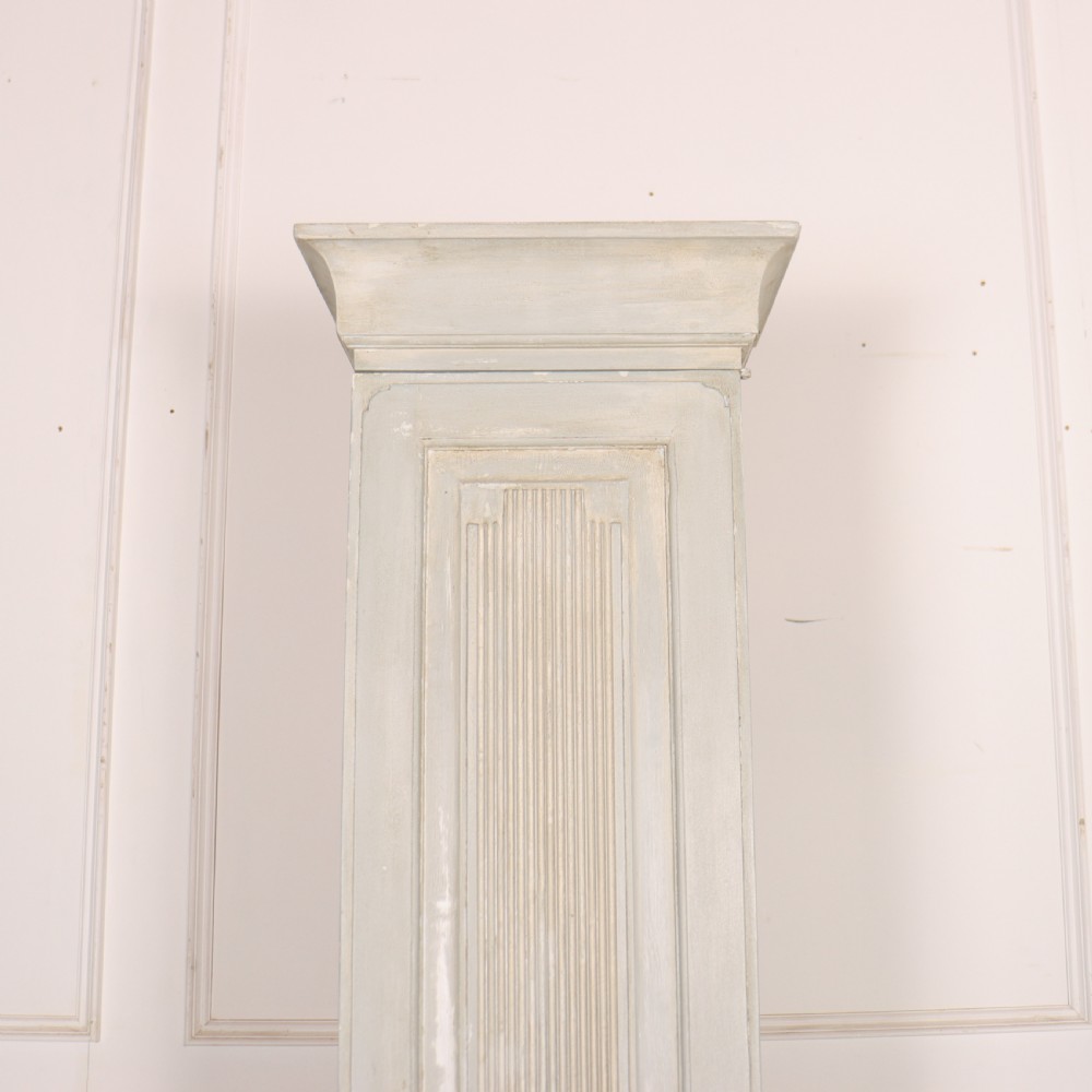 A tall, narrow Gustavian style two-tier painted wooden cabinet in pale grey with fluted panel doors and tapered feet. View VIII