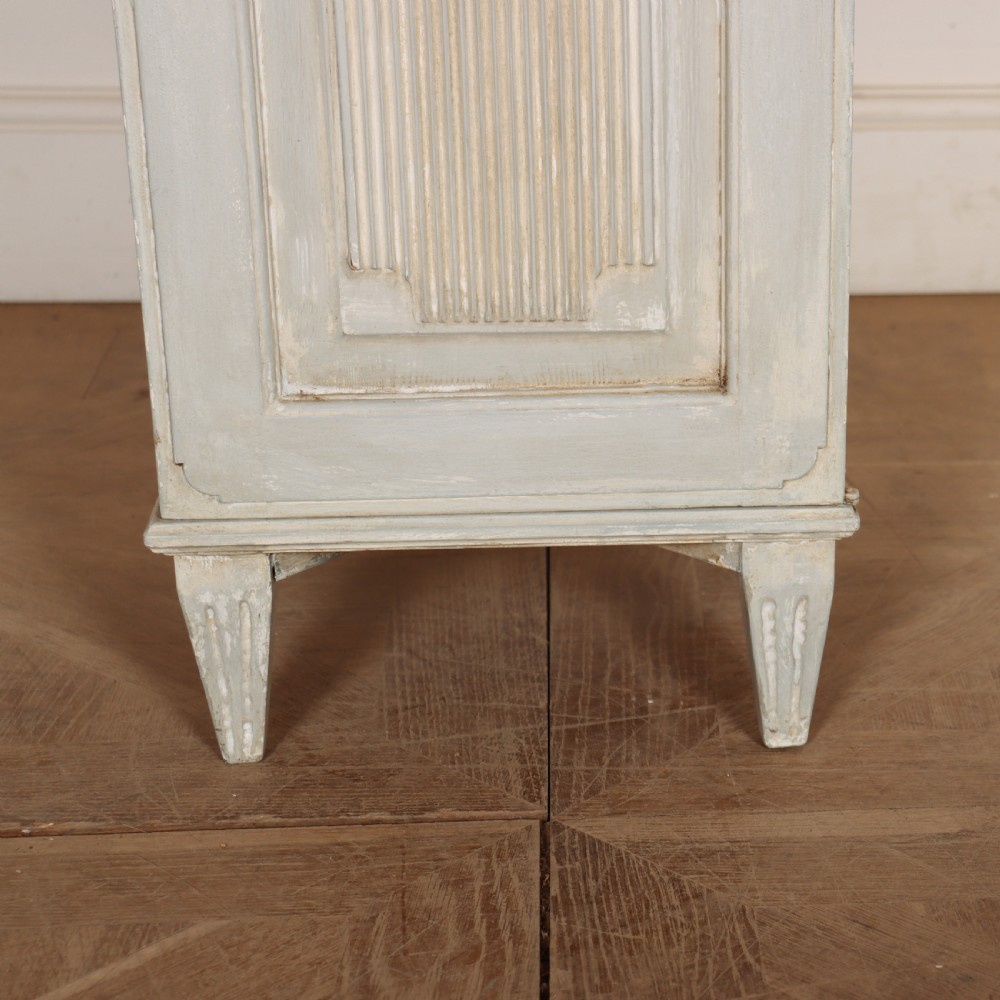 A tall, narrow Gustavian style two-tier painted wooden cabinet in pale grey with fluted panel doors and tapered feet. View IX