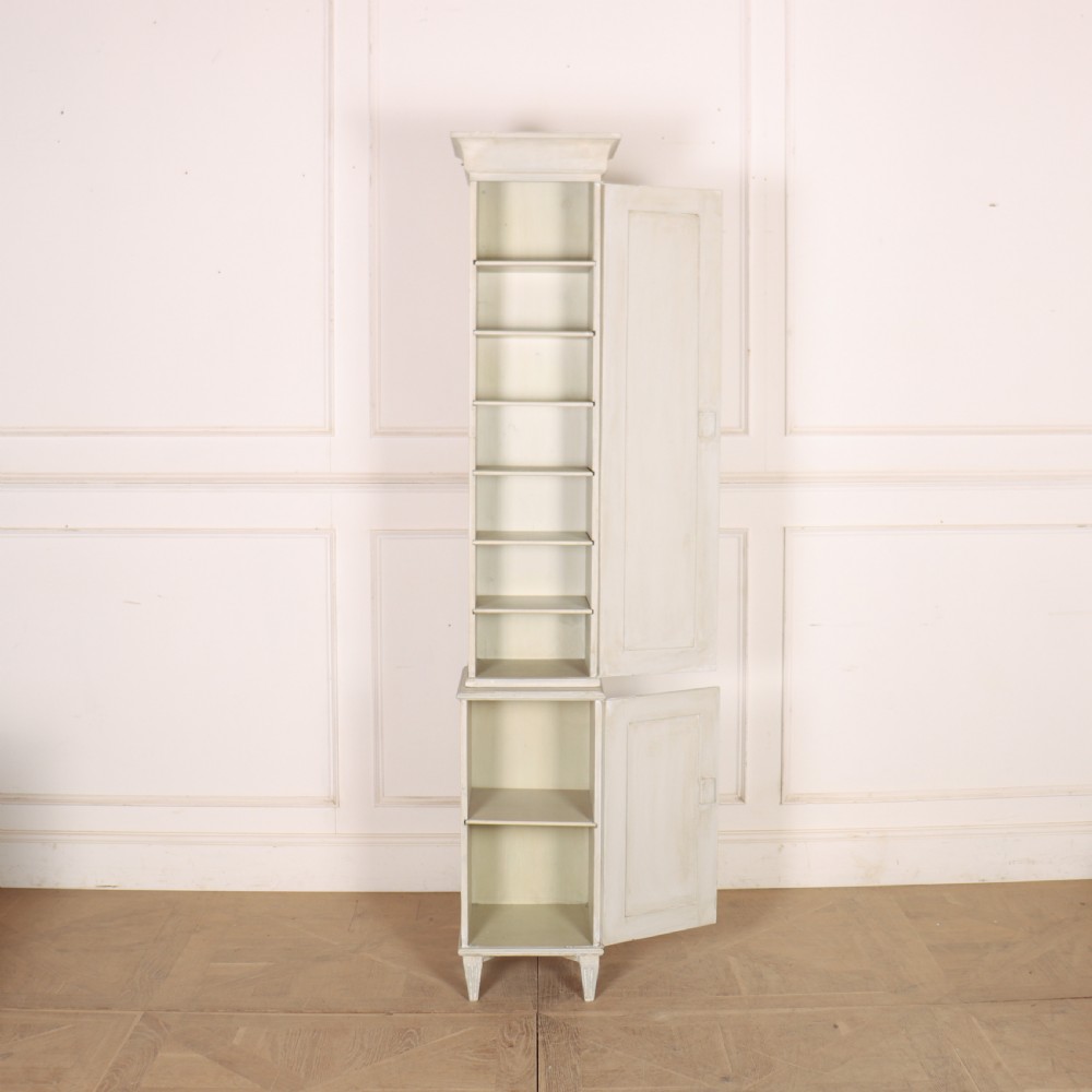 A tall, narrow Gustavian style two-tier painted wooden cabinet in pale grey with fluted panel doors and tapered feet. View X
