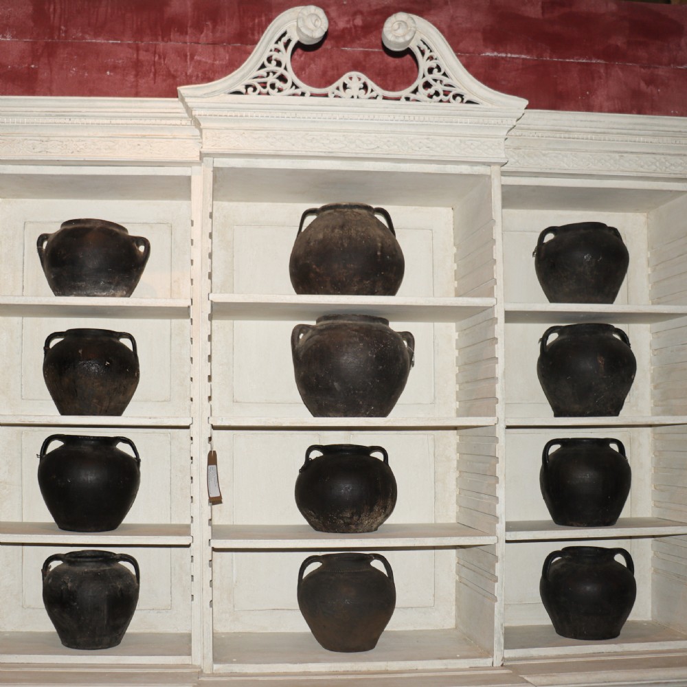 A collection of dark bulbous terracotta storage pots with small twin handles displayed on white shelving.