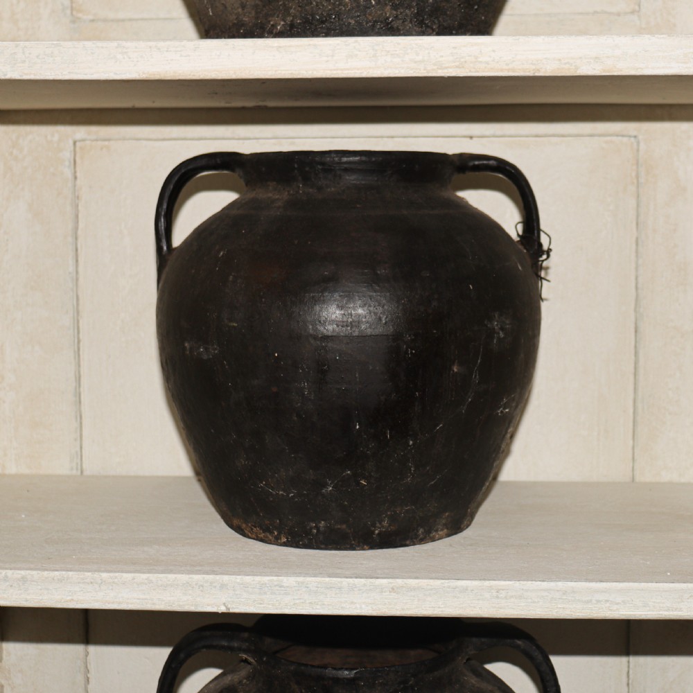 A collection of dark bulbous terracotta storage pots with small twin handles displayed on white shelving. View III