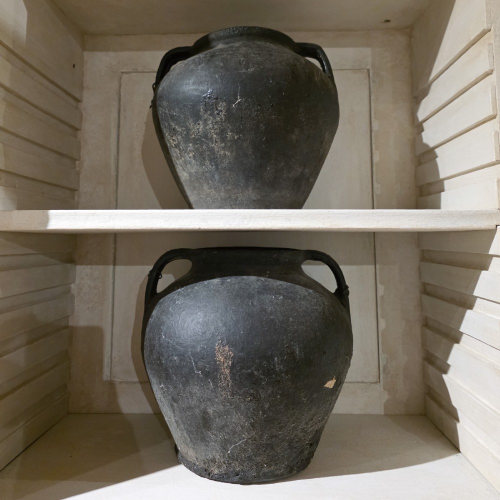 A collection of dark bulbous terracotta storage pots with small twin handles displayed on white shelving. View V