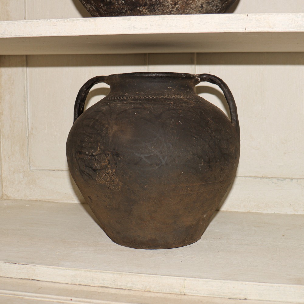 A collection of dark bulbous terracotta storage pots with small twin handles displayed on white shelving. View VI