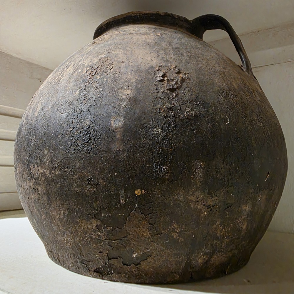 A collection of dark bulbous terracotta storage pots with small twin handles displayed on white shelving. View VII