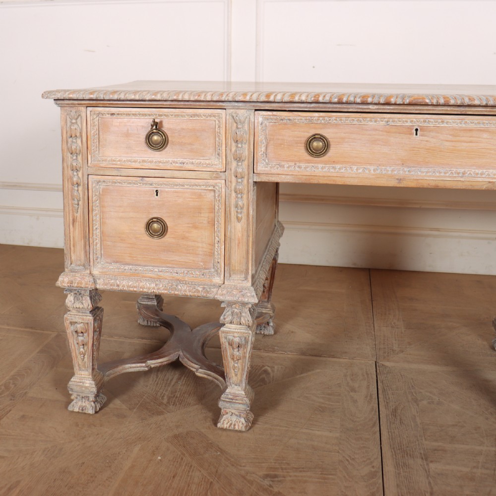 A pale bleached oak kneehole writing desk with intricate carved legs, five drawers with brass drop handles, and double X-frame stretchers. View II