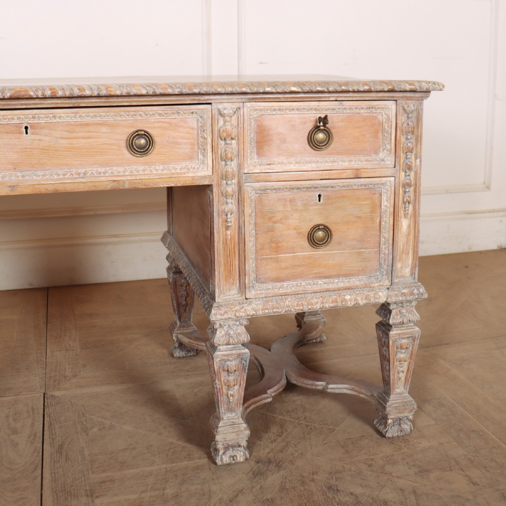 A pale bleached oak kneehole writing desk with intricate carved legs, five drawers with brass drop handles, and double X-frame stretchers. View III