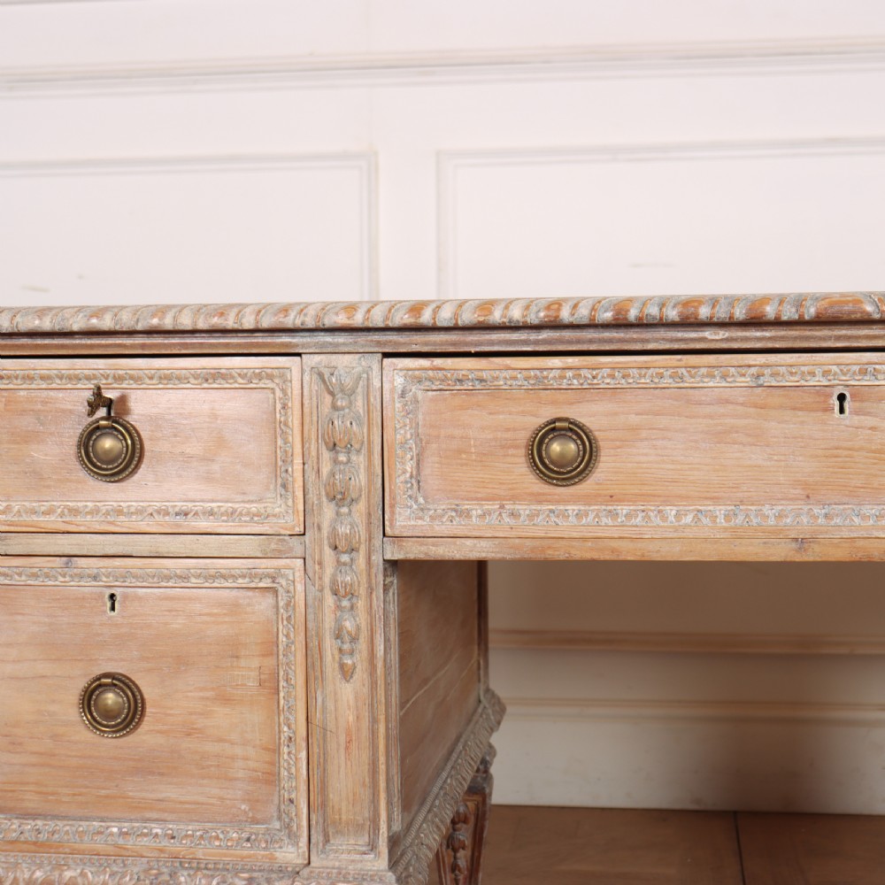 A pale bleached oak kneehole writing desk with intricate carved legs, five drawers with brass drop handles, and double X-frame stretchers. View VII