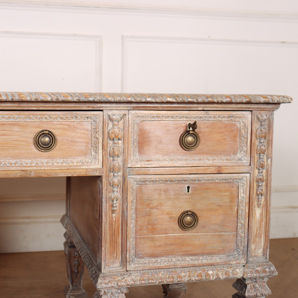A pale bleached oak kneehole writing desk with intricate carved legs, five drawers with brass drop handles, and double X-frame stretchers. View VIII