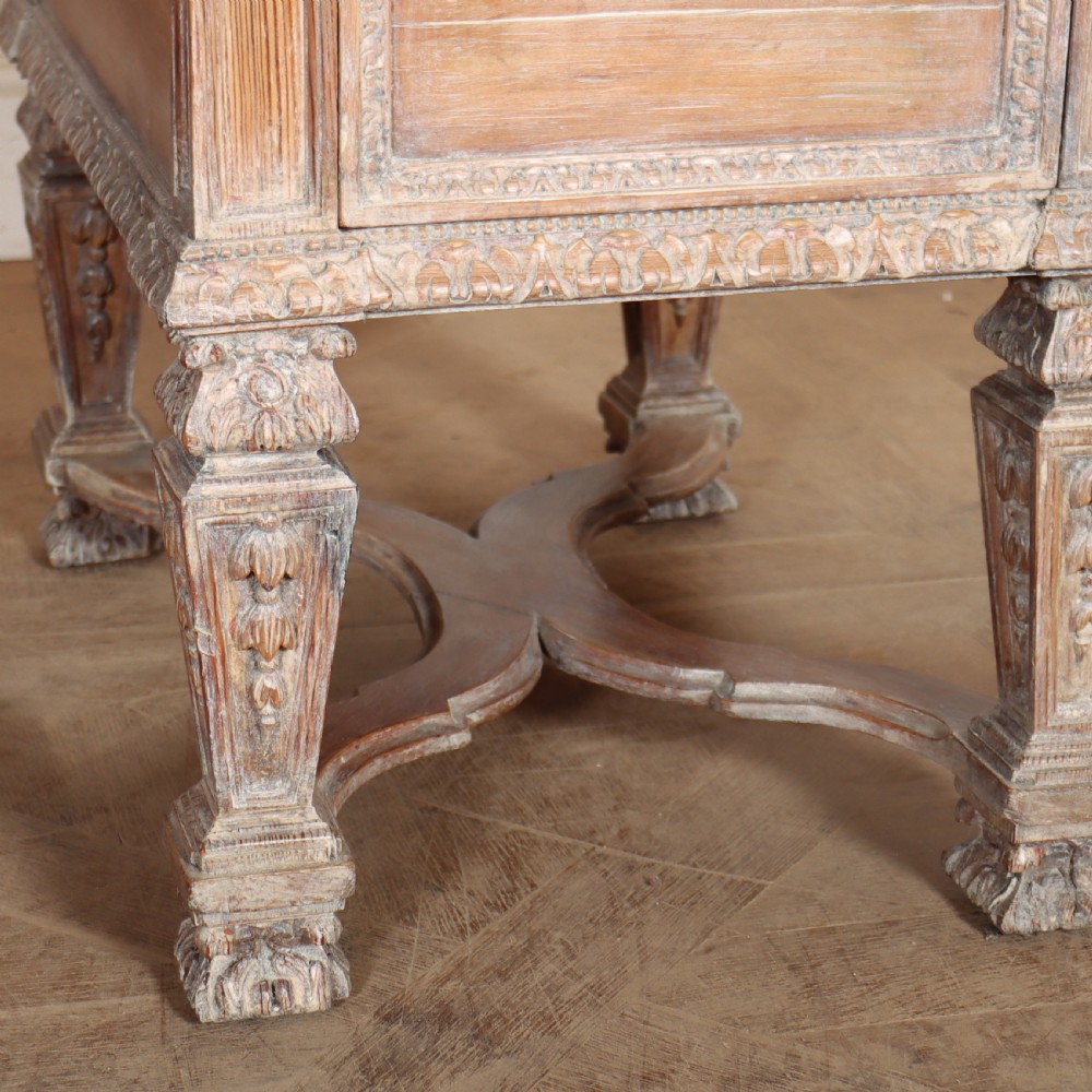 A pale bleached oak kneehole writing desk with intricate carved legs, five drawers with brass drop handles, and double X-frame stretchers. View X