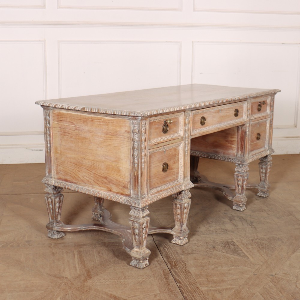 A pale bleached oak kneehole writing desk with intricate carved legs, five drawers with brass drop handles, and double X-frame stretchers. View XII
