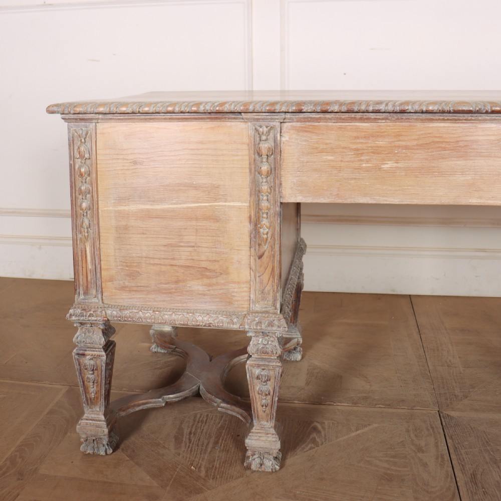 A pale bleached oak kneehole writing desk with intricate carved legs, five drawers with brass drop handles, and double X-frame stretchers. View XV