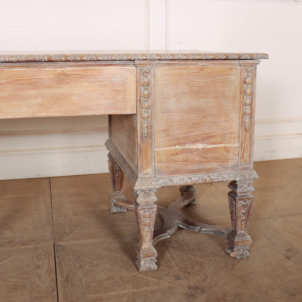 A pale bleached oak kneehole writing desk with intricate carved legs, five drawers with brass drop handles, and double X-frame stretchers. View XVI
