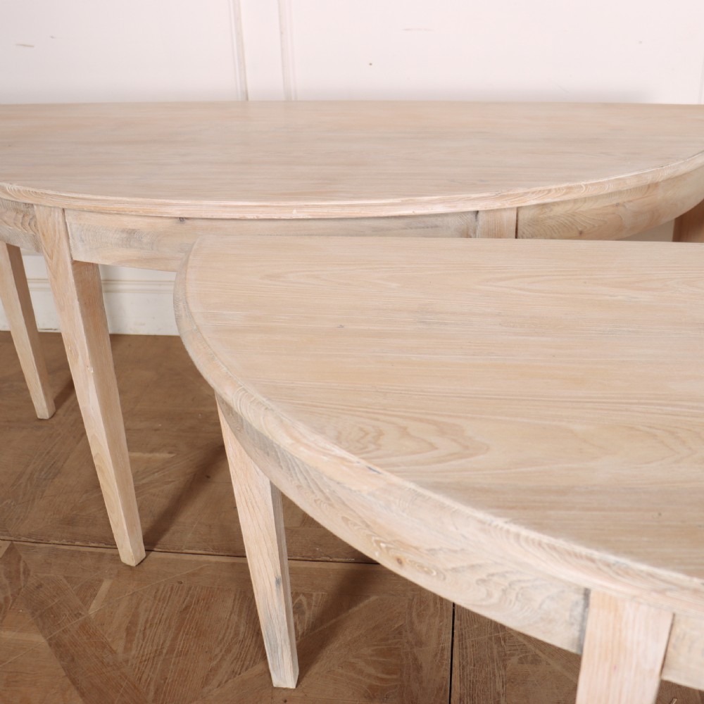 A pair of semi-circular, pale off-white painted console tables with tapered legs and flat backs designed to sit flush against a wall. View VI