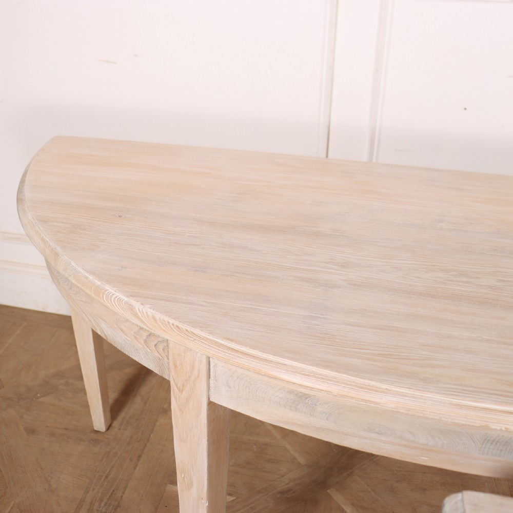 A pair of semi-circular, pale off-white painted console tables with tapered legs and flat backs designed to sit flush against a wall. View VIII