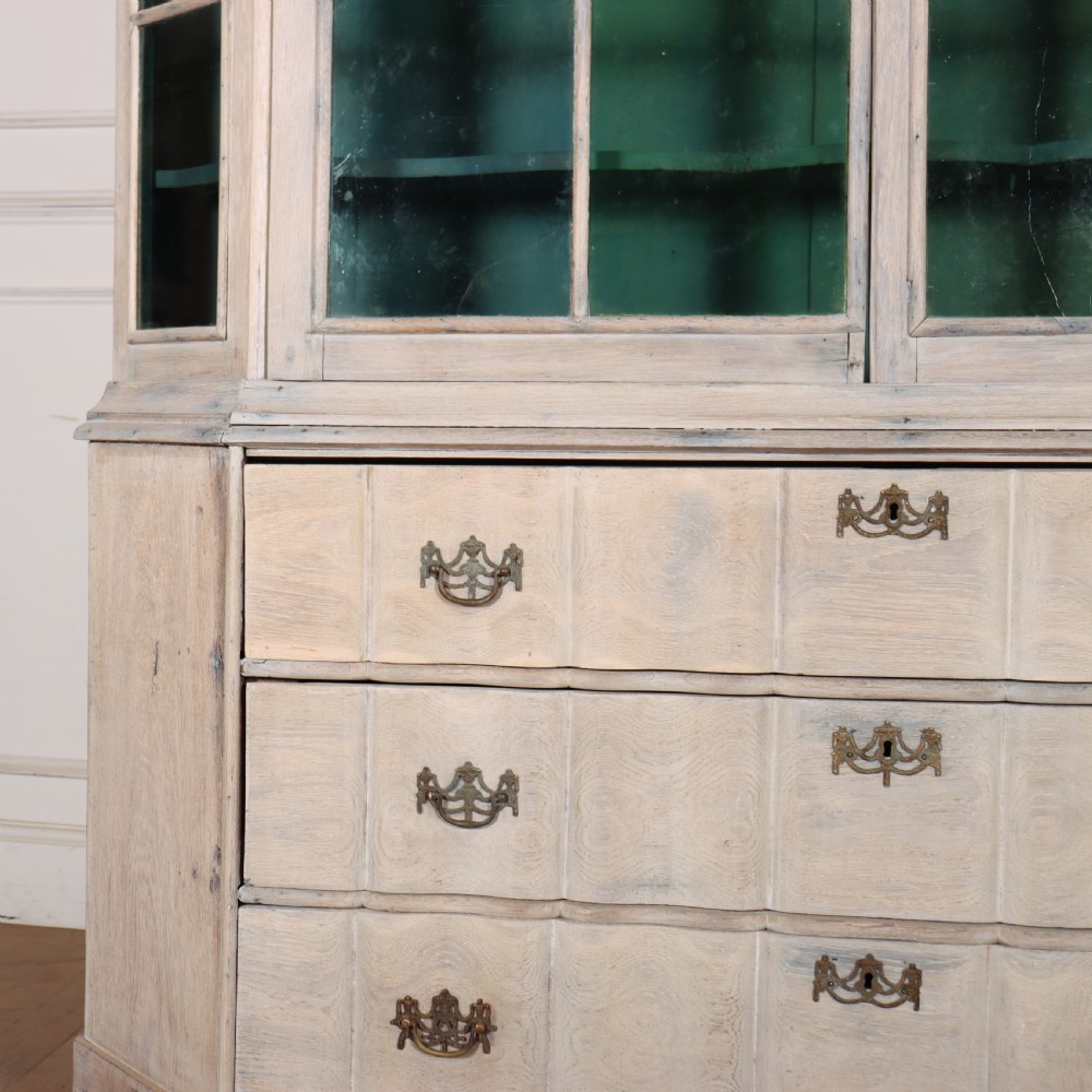 An antique Dutch glazed display cabinet with a grey-washed exterior, green painted interior, curved cresting rail, and three drawers in the base. View V