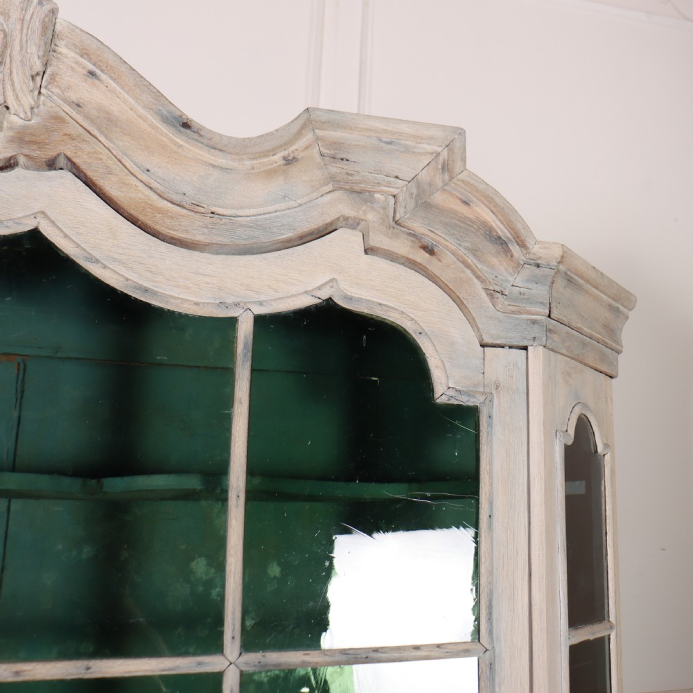 An antique Dutch glazed display cabinet with a grey-washed exterior, green painted interior, curved cresting rail, and three drawers in the base. View VIII