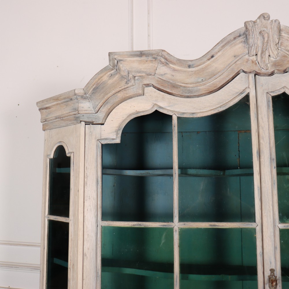 An antique Dutch glazed display cabinet with a grey-washed exterior, green painted interior, curved cresting rail, and three drawers in the base. View IX