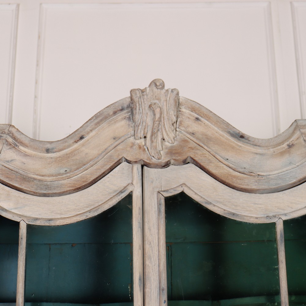 An antique Dutch glazed display cabinet with a grey-washed exterior, green painted interior, curved cresting rail, and three drawers in the base. View X