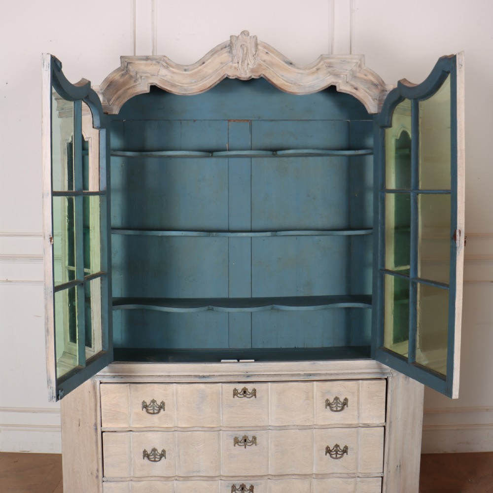 An antique Dutch glazed display cabinet with a grey-washed exterior, green painted interior, curved cresting rail, and three drawers in the base. View XI