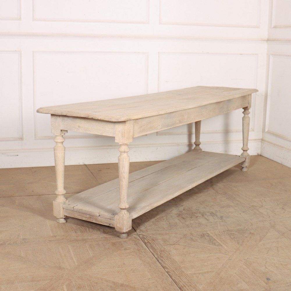 A long bleached oak French drapers table featuring turned legs and a full-length lower tier shelf.