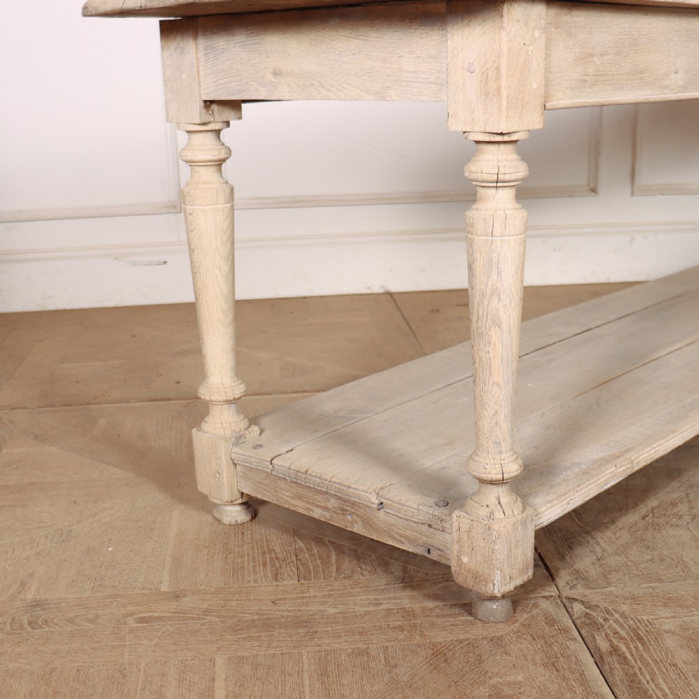 A long bleached oak French drapers table featuring turned legs and a full-length lower tier shelf. View II