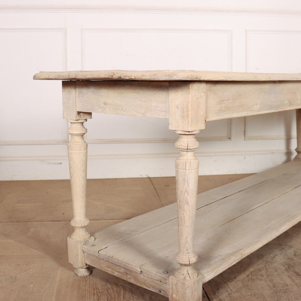 A long bleached oak French drapers table featuring turned legs and a full-length lower tier shelf. View III