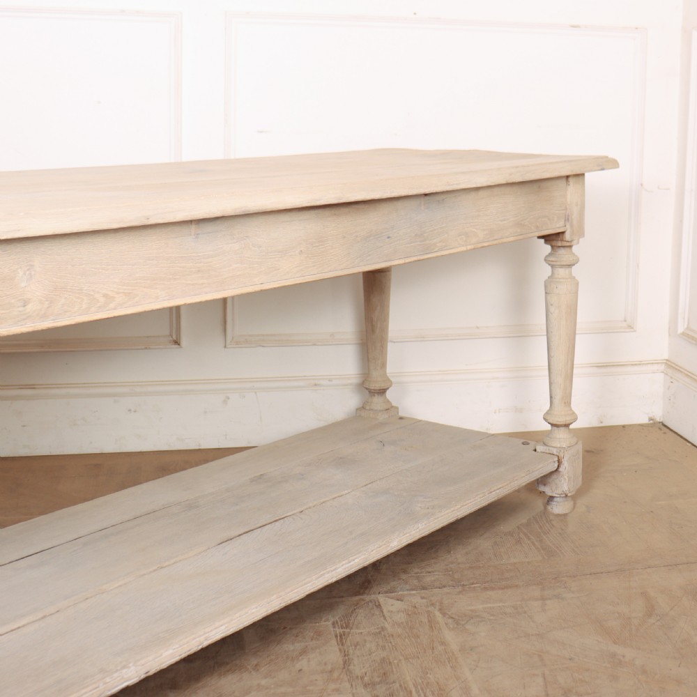 A long bleached oak French drapers table featuring turned legs and a full-length lower tier shelf. View IV