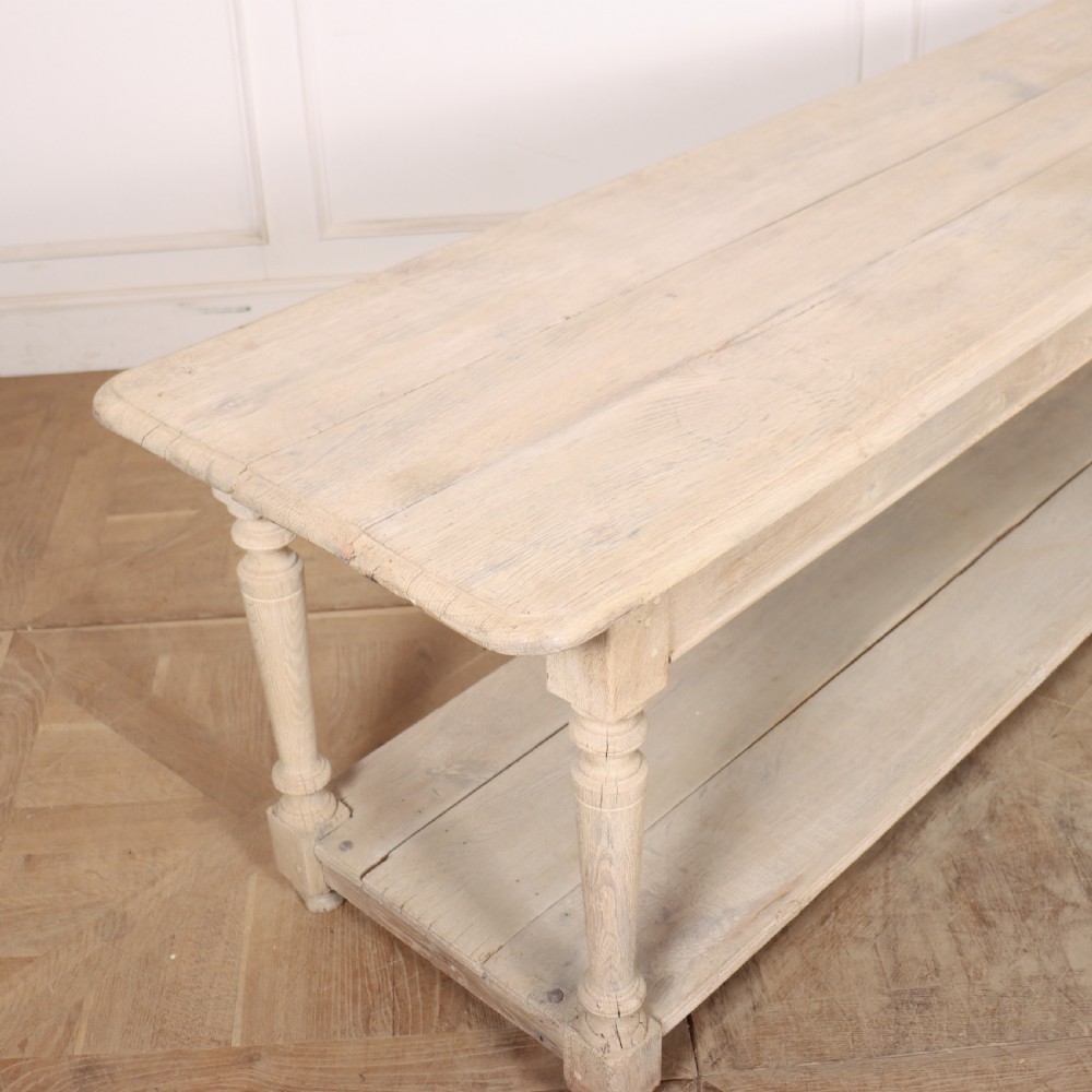 A long bleached oak French drapers table featuring turned legs and a full-length lower tier shelf. View V