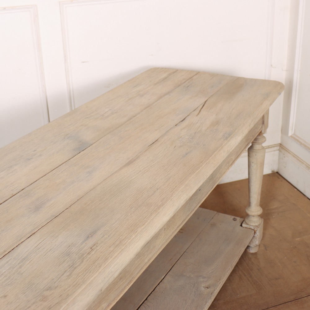 A long bleached oak French drapers table featuring turned legs and a full-length lower tier shelf. View VI